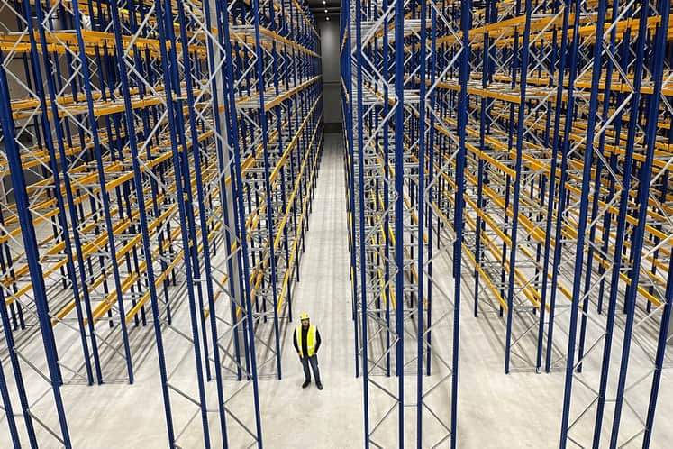 En man står i en lagerlokal med höga pallplatser.