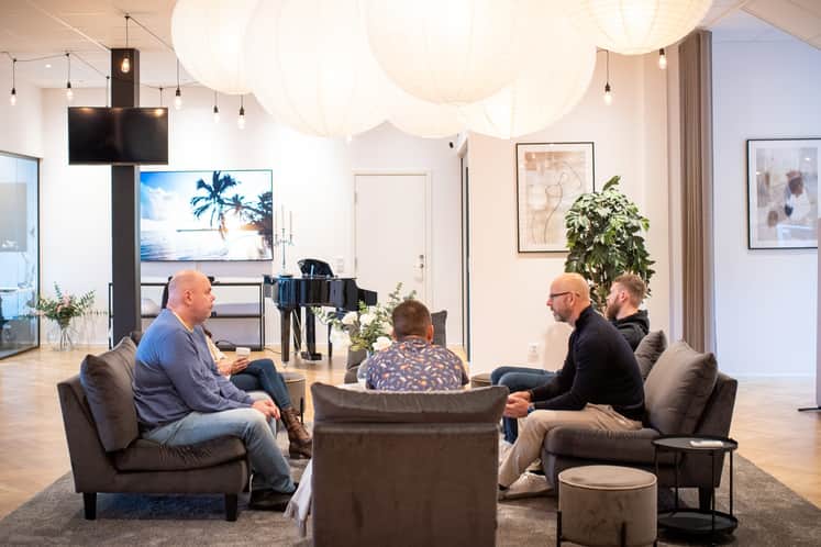 Medarbetare sitter i soffor och pratar, en flygel i bakgrunden.