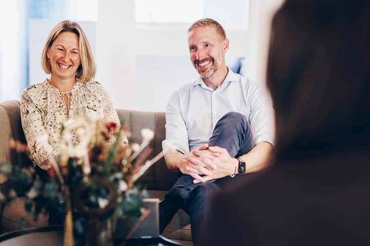 En man och en kvinna sitter och pratar i en soffa med en person mitt emot