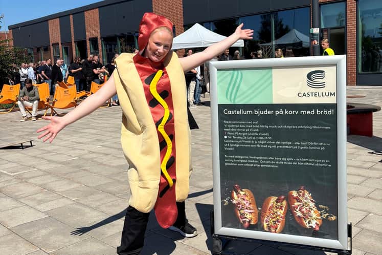 Kvinna utklädd till korv med ringlande kö i bakgrunden