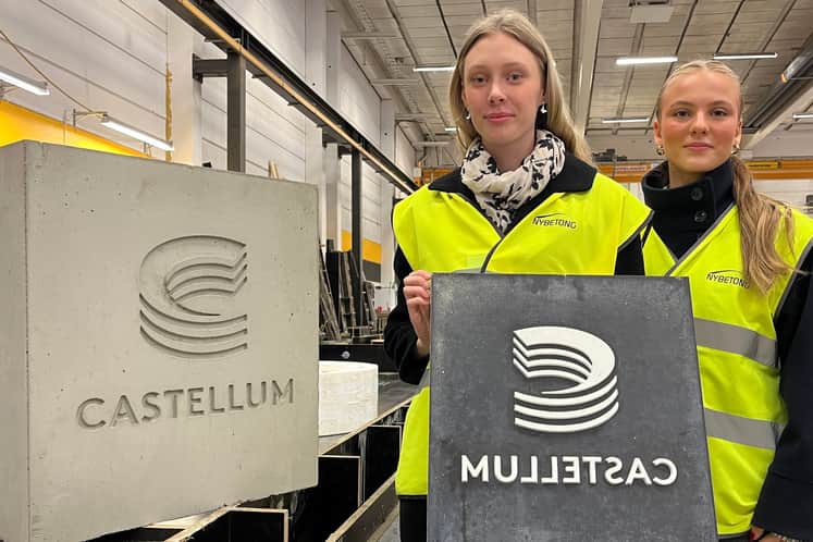 Två unga tjejer med gul arbetarväst på sig som sitter på huk med en betongplatta framför sig som är en del av bänkarna de skapar.