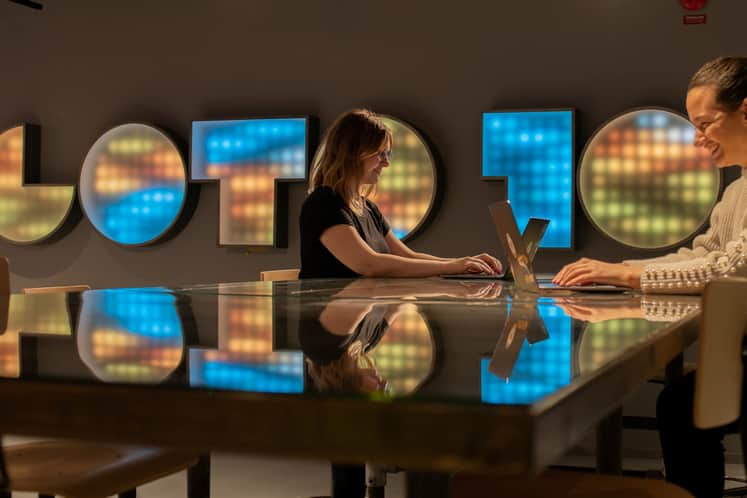 Två personer med varsin lapotop står vid ett högt bord framför en vägg med texten Goto 10.