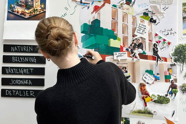 En tjej står med ryggen vänd framför en moodboard och skriver på tavlan.