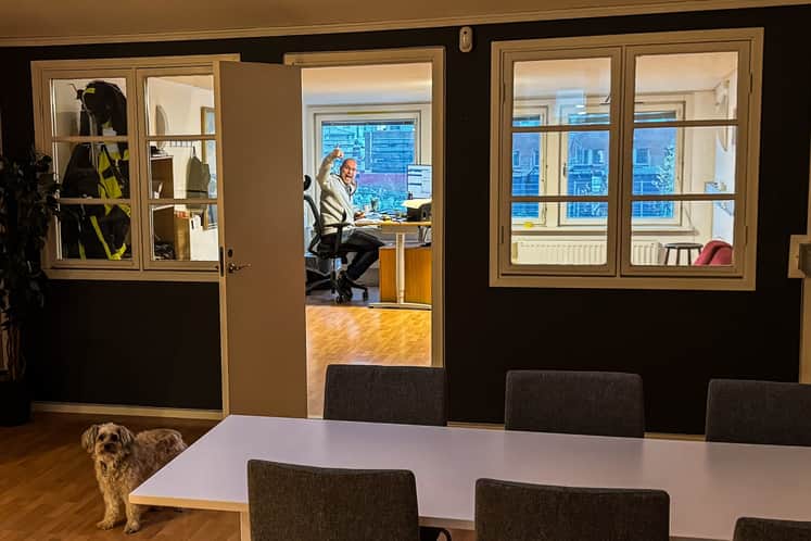 Ett rum med bord, stolar och en hund. En man vinkar