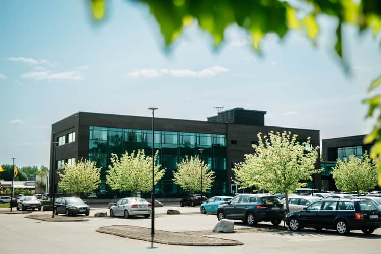 Svart byggnad med gröna blommande träd framför och en parkering