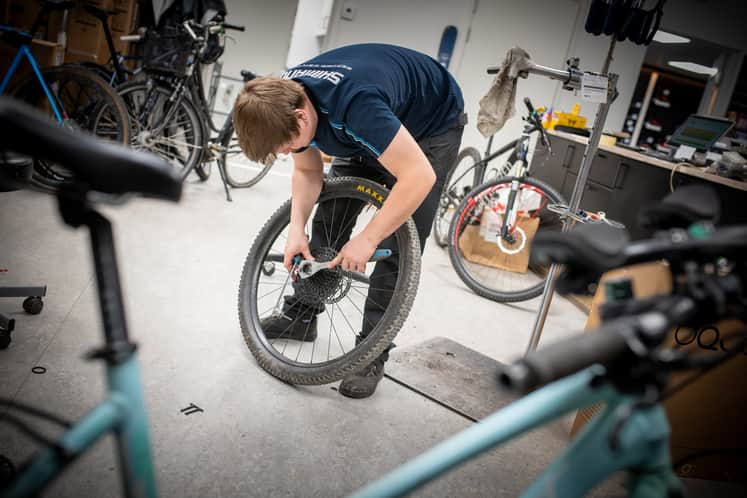 Person som står lutad över ett cykeldäck och skruvar navet