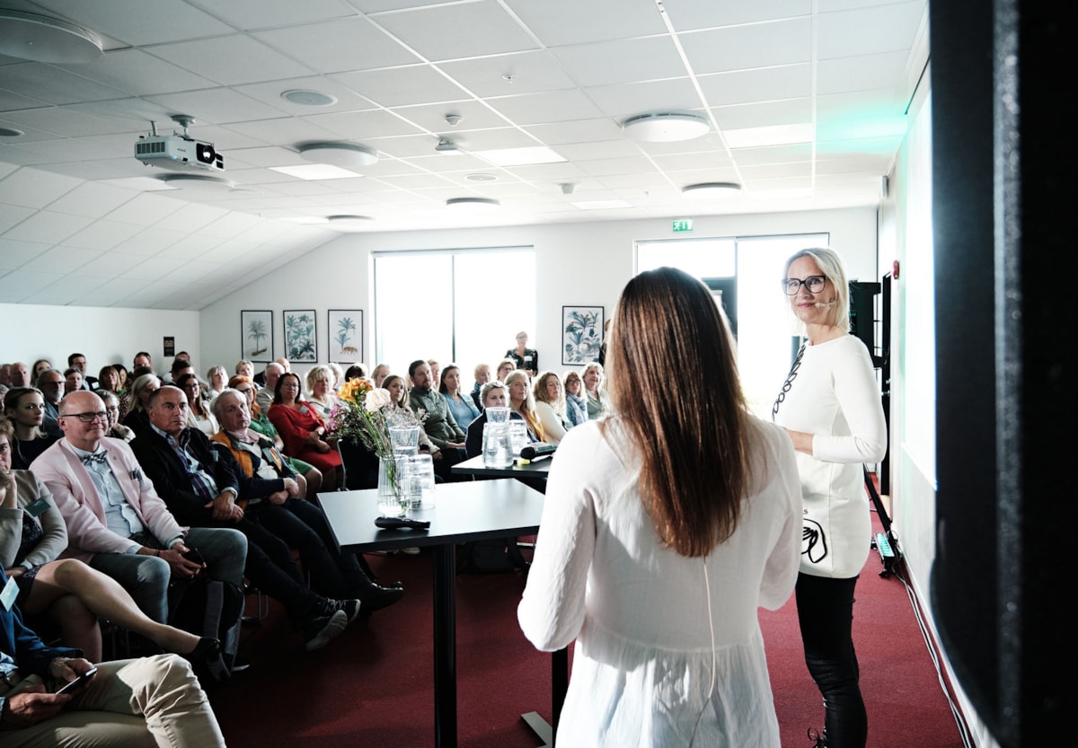 sittandes m&auml;nniskor i ett m&ouml;tesrum, till h&ouml;ger st&aring;r tv&aring; f&ouml;rel&auml;sare. 