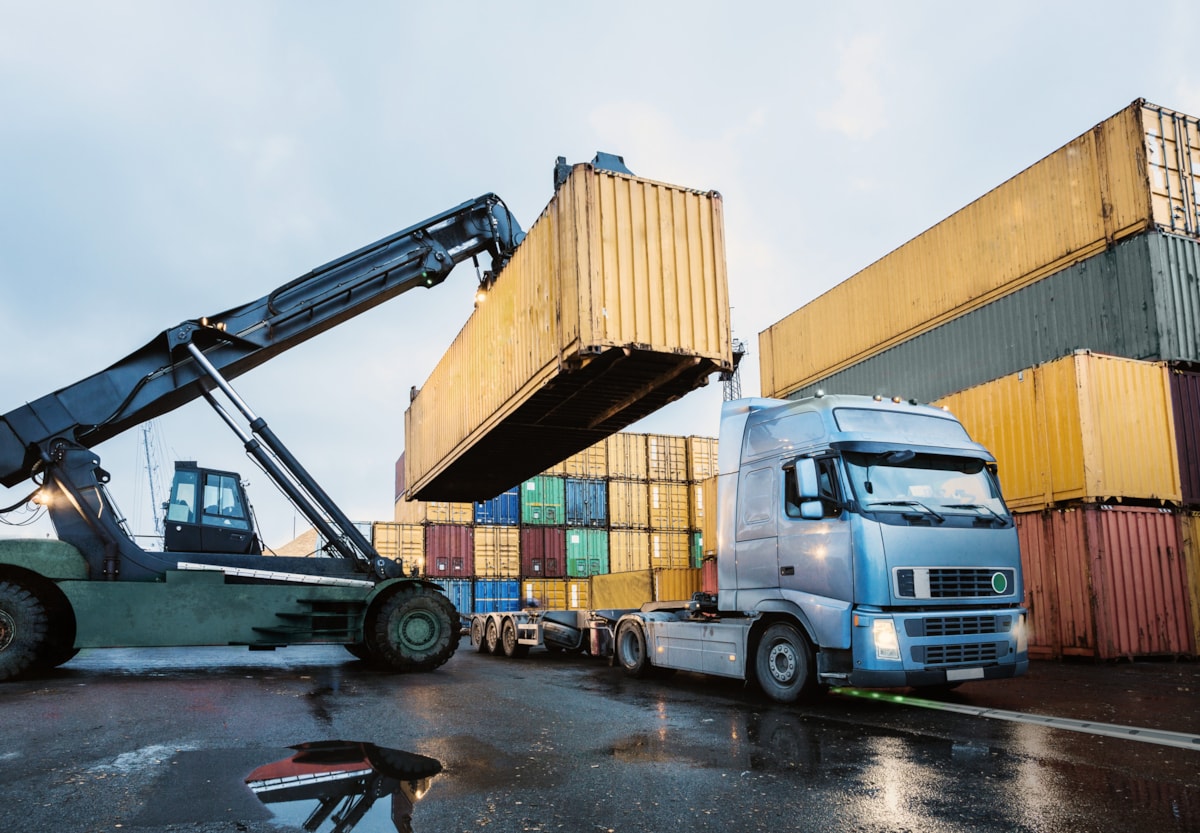 Lastbil och flera containrar, en container lastas p&aring; lastbilen