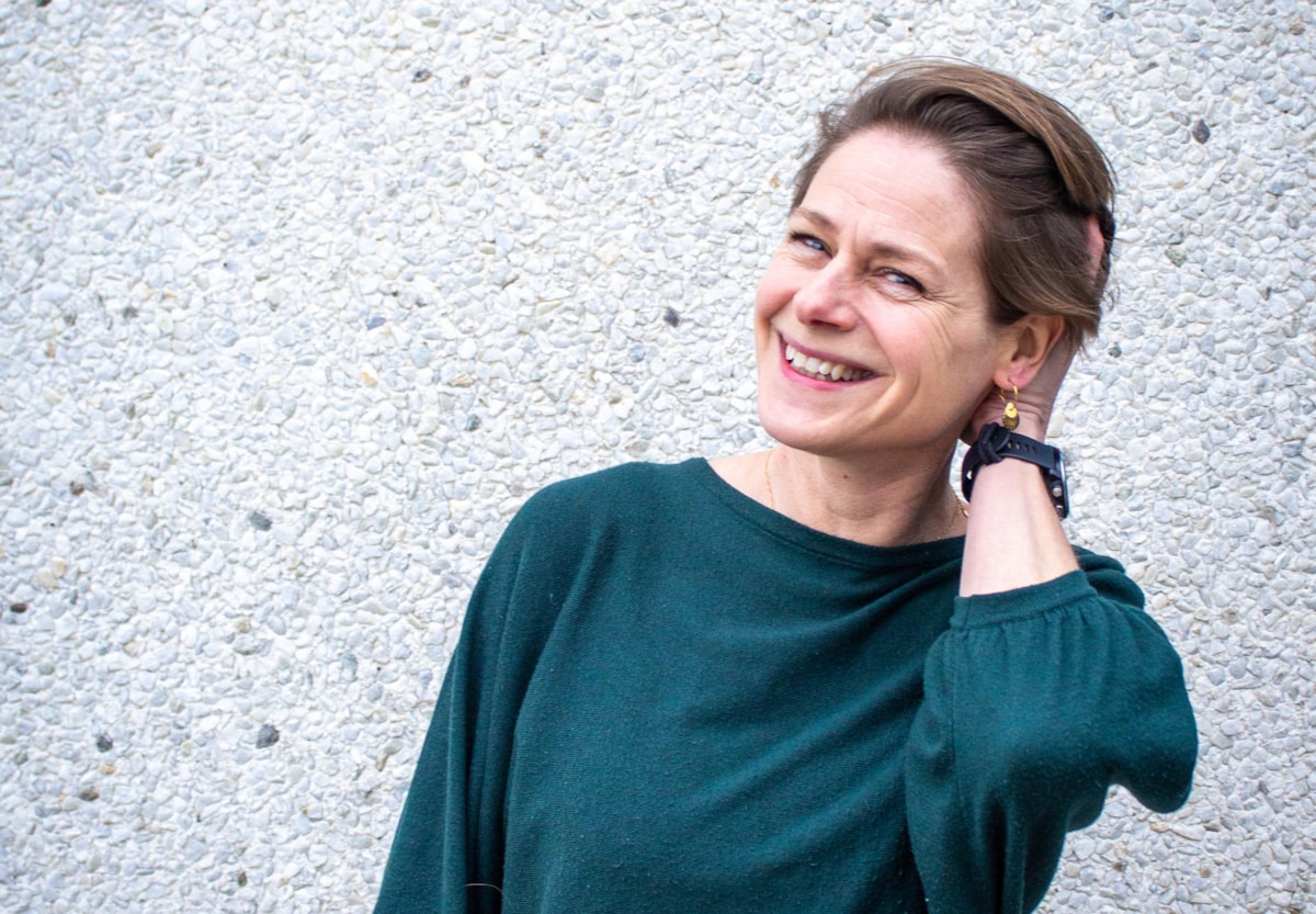 En portr&auml;tt p&aring; en person, personen ler och lutar mot h&ouml;ger och h&aring;ller ena handen i h&aring;ret