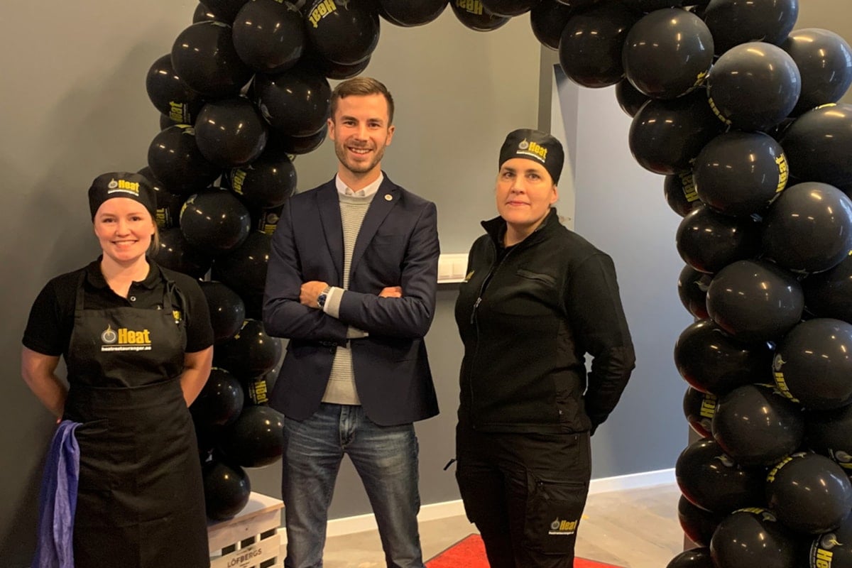 Tre personer under en b&aring;ge av svarta ballonger.