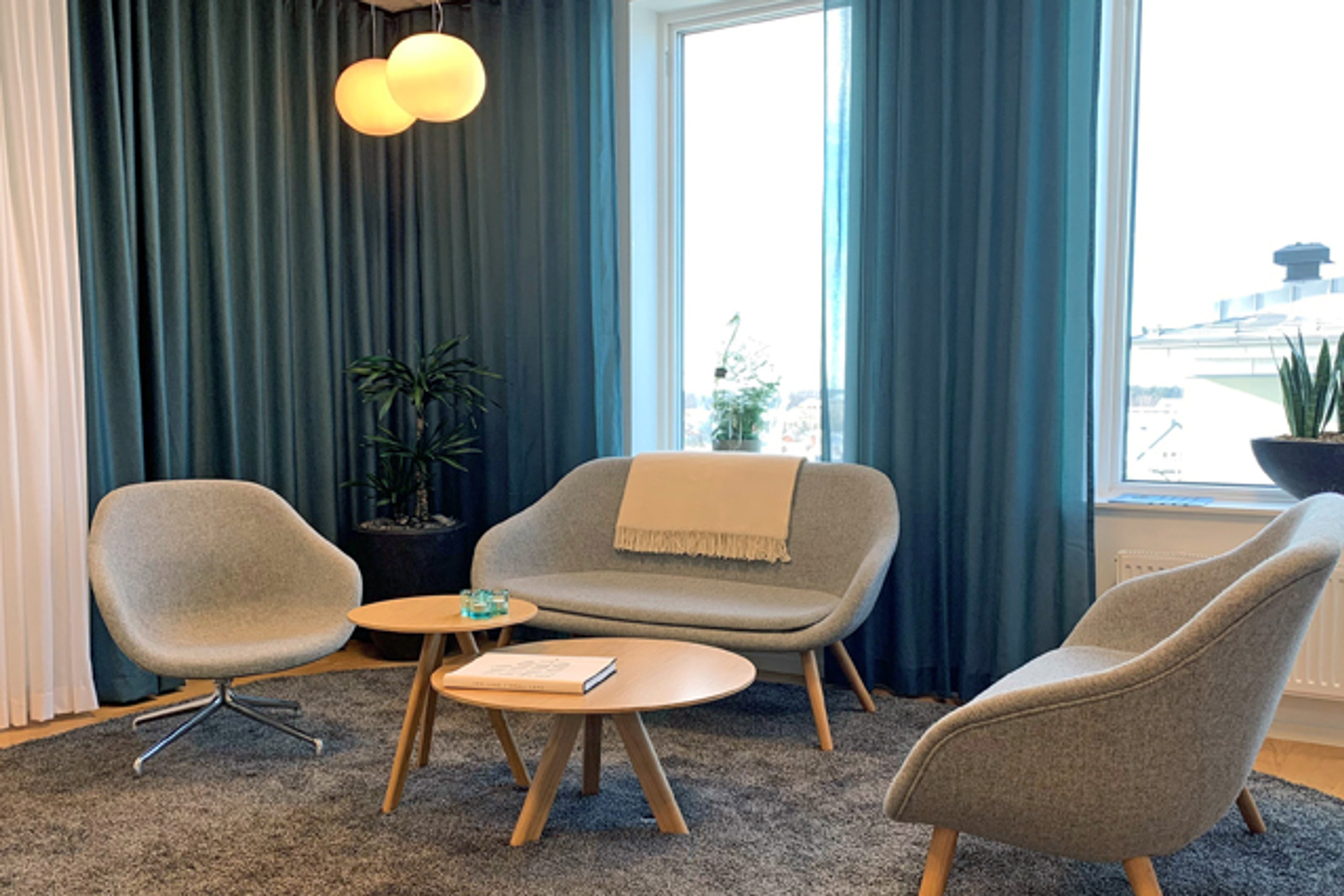 Gr&aring; soffgrupp framf&ouml;r f&ouml;nster med bl&aring; gardiner.